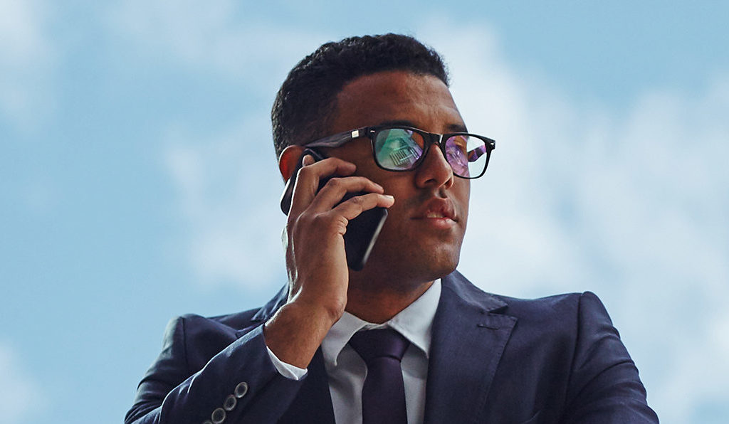 Young businessman speaking on mobile phone against cloudy sky